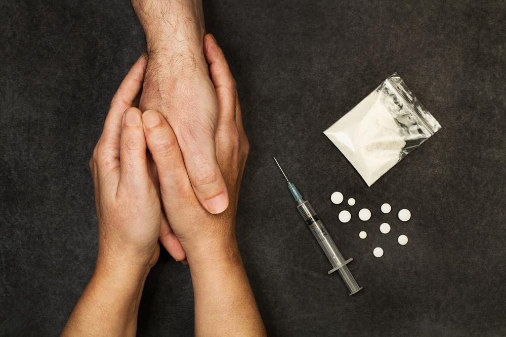 Woman holding a drug addict's hands, with drugs nearby