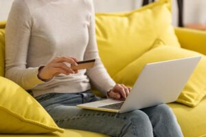 Woman sitting on a sofa doing online shopping on a laptop and holding a credit card