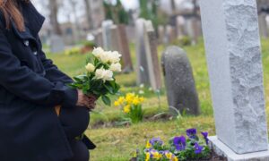 Mourner grieving at a graveside putting some flowers on a grave