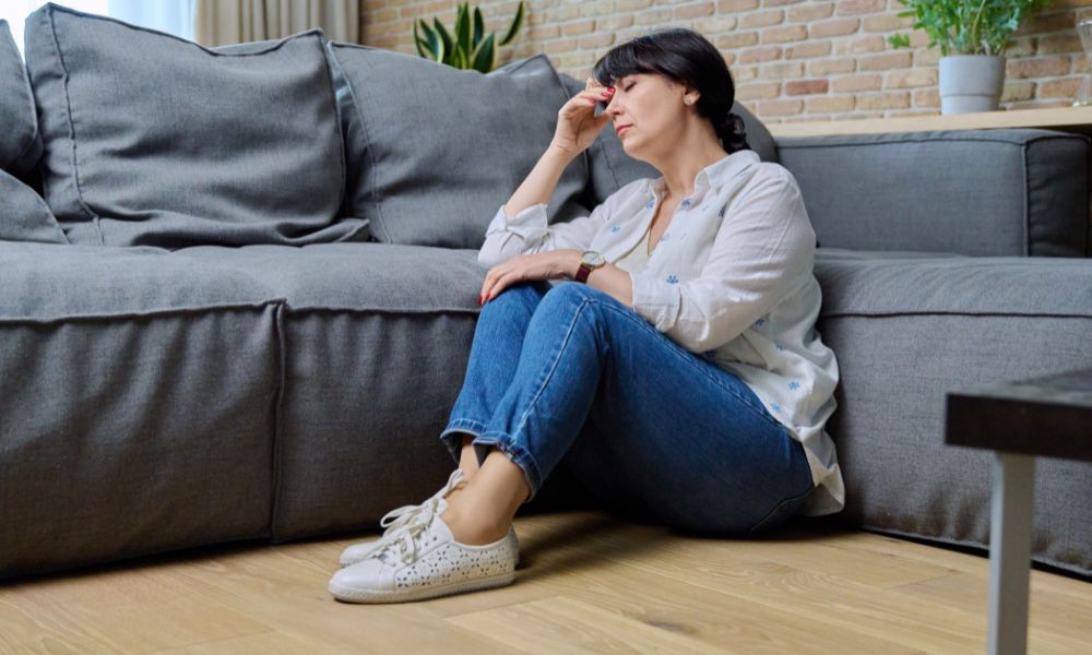 An older lady sitting on the floor in her lounge looking very sad.